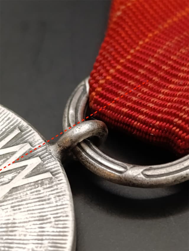 Uszko przymocowane niesymetrycznie, zamiast nad środkową literą X jest przesunięte